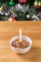 The cereal in the white bowl is on the wooden table and Christma