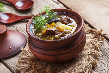 Soup with mushrooms, beef and barley, clay pots, vintage wooden