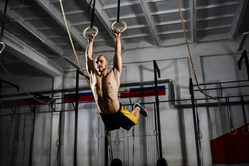 Muscle-up exercise athletic man doing intense workout at the gym on gymnastic rings