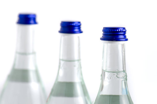 3 Glass Bottles In Row Filled With Soda Water With Blue Caps Iso