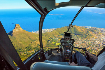 Naklejka premium Kokpit helikoptera leci w Lion's Head, na wybrzeżu iw Kapsztadzie w RPA, z ramieniem pilota i tablicą kontrolną wewnątrz kabiny.