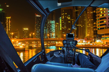 Helicopter cockpit flies in Dubai Marina by night, United Arab Emirates, with pilot arm and control board inside the cabin.