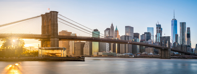 The panorama view of Brooklyn Bridge with Lower Manhattan in the background, lit by sunset - obrazy, fototapety, plakaty