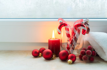 Christmas scene with one burning candle and christmas decorations on winter fozen windowsill