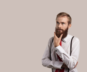 Portrait of Dreaming person. Handsome man thinking and look up. Guy keep beard by one hand. Stylish hipster look with white shirt and red tie. Copy space for text.