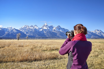 Rear view of a blurred woman taking pictures with DSLR camera in the Grand Teton National Park, focus on background, Wyoming, USA.