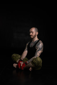 Relaxing man fighter before scramble. Handsome brutal guy with short breard black shirt and hexagonal camouflage trousers. Sport concept for health life.