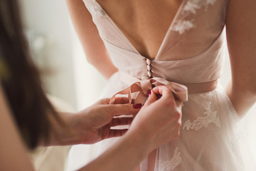 Closeup of bridesmaid tying bow on bride's dress - obrazy, fototapety, plakaty