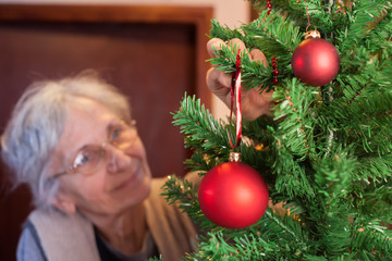 old woman putting ornaments on Christmas tree