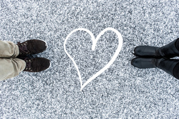 Men and women's boots standing at abstract heart symbol on asphalt covered gritty snow surface....
