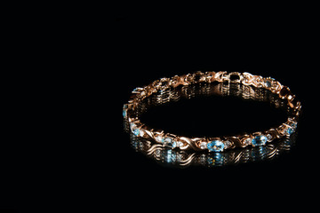 Golden bracelet with gems and topaz and diamonds on black background in studio