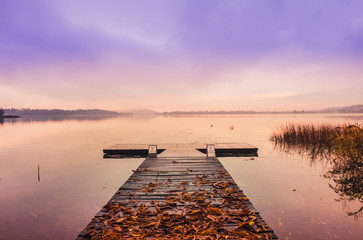 Wooden pier with leaves on the quiet lake at sunrise in autumn