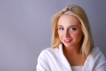 Naklejka premium Smiling woman in white bathrobe, isolated on gray background
