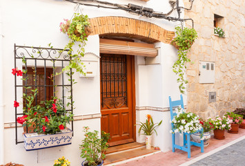 Fototapeta na wymiar Chair and flower pots decorate home exterior in narrow Spanish street
