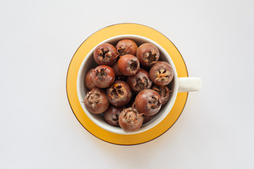 white bowl on a yellow saucer full of sweet medlar on a white background