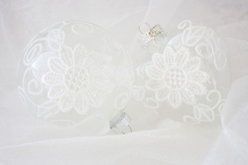 horizontal image of two clear glass Christmas ornaments decorated with white lace on a white sheer nylon background.