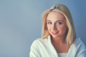 Naklejka premium Smiling woman in white bathrobe, isolated on gray background