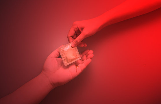 Woman's hand giving man's hand a gold condom with color filter, safe sex concept