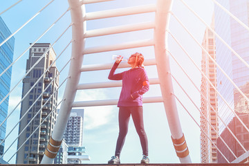 Sporty young woman drinking water in the tower background