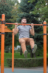 Obraz premium young man doing pull ups on horizontal bar outdoors.