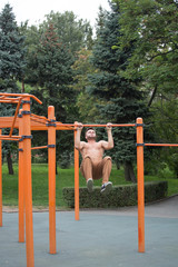 Obraz premium young man doing pull ups on horizontal bar outdoors.