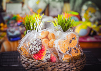 Plastic disposable containers with cookies and pastries in a wicker wooden basket on a motley, colored background