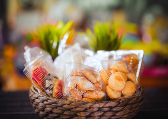 Plastic disposable containers with cookies and pastries in a wicker wooden basket on a motley, colored background