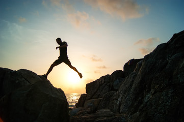 Man jump through the gap between hill.man jumping over cliff on sunset background,Business concept...