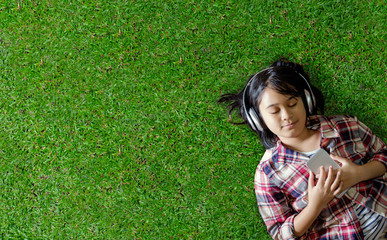 Pretty young Asian girl lying on grassland and listening music.