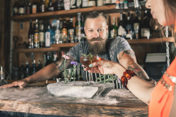 Beautiful girl is drinking a cocktail with ice vapor in the bar