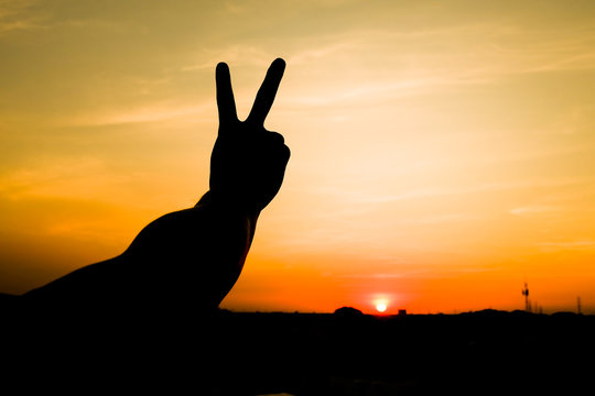 The silhouette of a man holding up two fingers to the sky at sunset. , A symbol of peace and victory, or fighting.