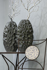 two dark vase with curves and a silver branch on the table against the background of a gray wall
