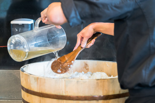 Mixing rice. Close up of cook hands mixing with long wooden spoon white rice in a wooden bowl
