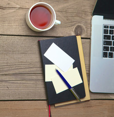Blank business cards with pen, laptop and tea cup on wooden office table