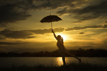 woman holding Umbrella at sunset moment near lake.cloudy sky and big mountain in background.silhouette.jump with umbrella at sunset