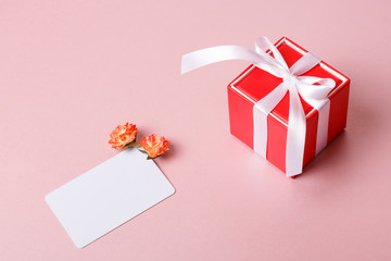 Valentine day composition: red gift box with bow, credit / visiting card template and spring flowers on light pink background.