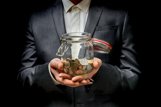Man in black suit holding money jar with coins