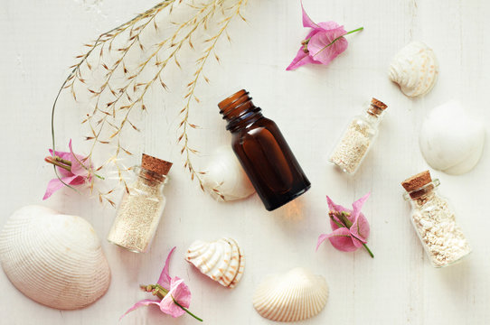 Essential oil, bottles with sand, sea shells, tropical flowers, top view white wooden spa treatment background. Relaxation set.