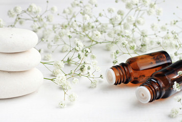 Obraz na płótnie Canvas Tranquil white aromatherapy setting. Dropper bottles of aroma herbal essence, green and white airy flower decor, spa stones.