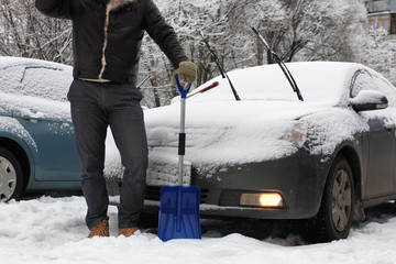 man cleans snow from a car on a winter morning