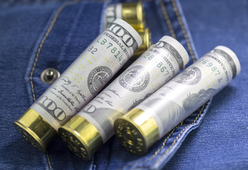 Fototapeta premium Several 12 caliber shotgun shells loaded with us hundred dollar bills on blue jeans pocket background.