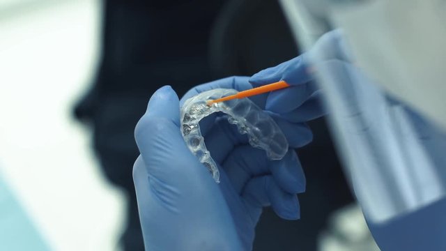 Close-up shot of doctors hands in gloves working with silicone mouth guard.