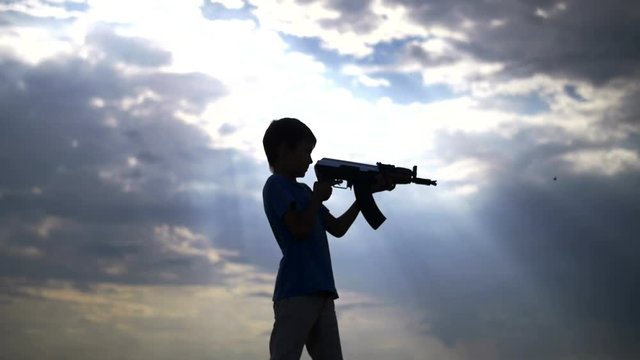 silhouette boy with a gun at sunset on the background of clouds, ak 47