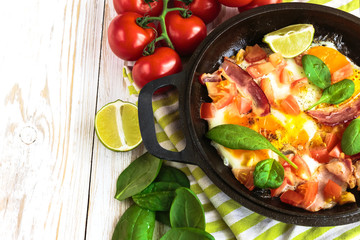 Pan of fried eggs with tomatoes, bacon, spinach, lime