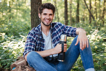 Obraz premium Guy sitting with thermos in forest