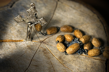 Silver crucifix and a rosary with wooden beads on a tree trunk