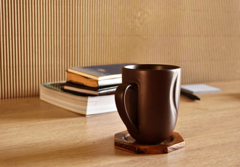 Brown coffee cup and books on a wooden table.