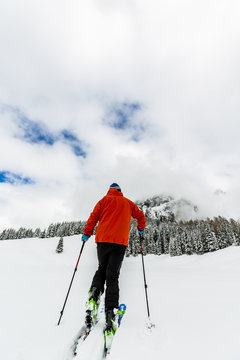Mountaineer standing up along a snowy ridge with skis. In backgr