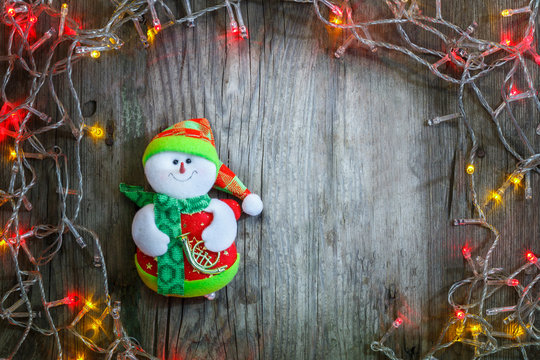 Colorful Christmas garland lights and smiling snowman on wooden rustic background. Christmas decorations. Holiday mood. Beautiful New Year composition.