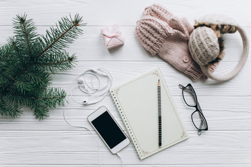 Woman hands in mittens and notebook with wish list on turquoise vintage table from above, christmas planning concept. Christmas decorations with notebook and smartphone. To do list.